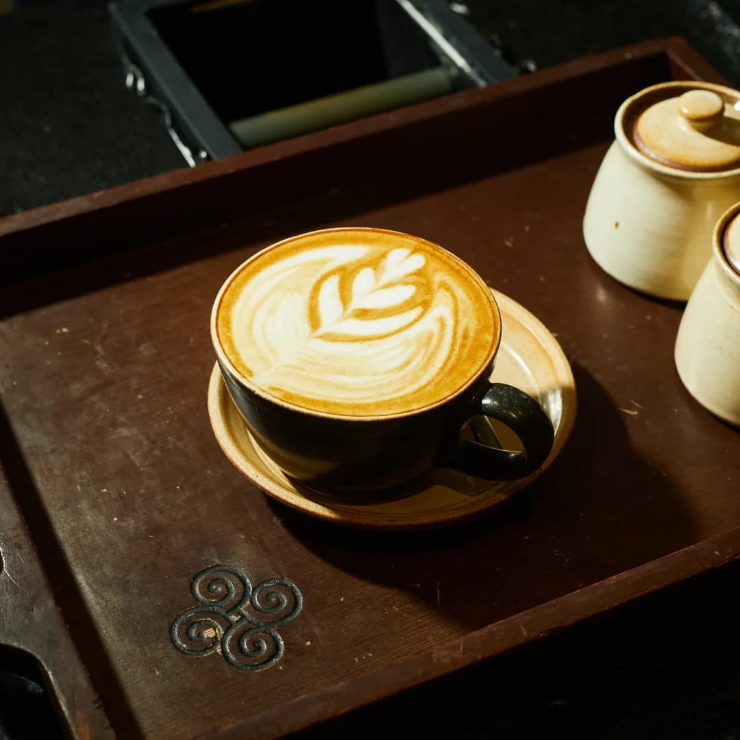 A rosetta poured into a flat white, served on ceramic atop the Les Amis wooden tray