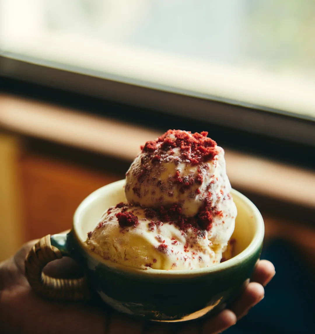 A hand holding a green ceramic cup of red-velvet gelato by the window