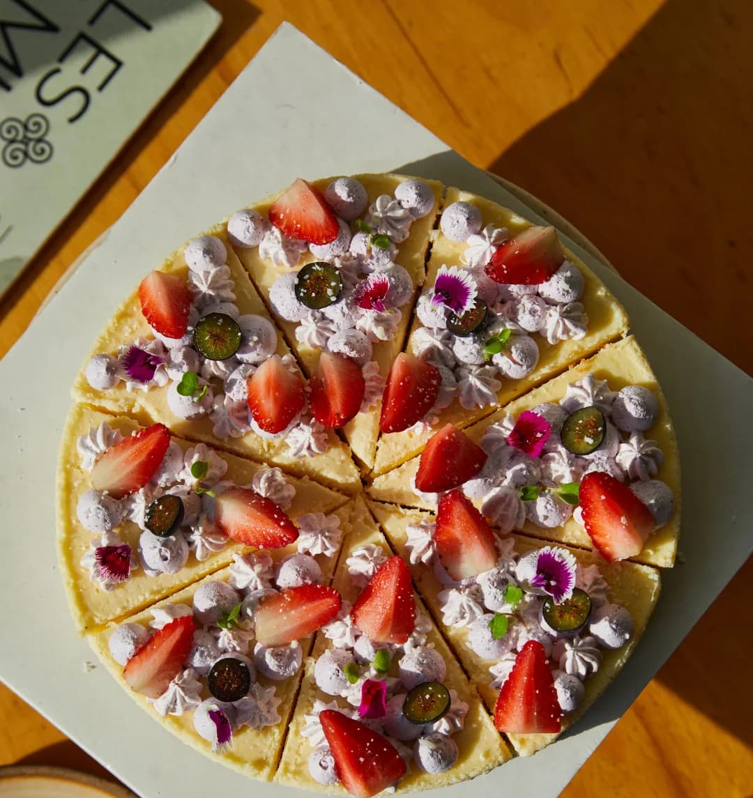 A whole cheesecake in golden light, sliced and finished with strawberries, blueberries and edible flowers