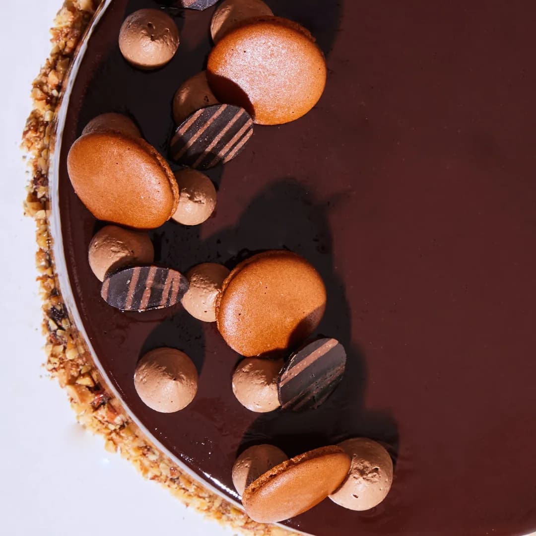 A mirror-glazed chocolate entremet edged with roasted nuts and topped with macarons