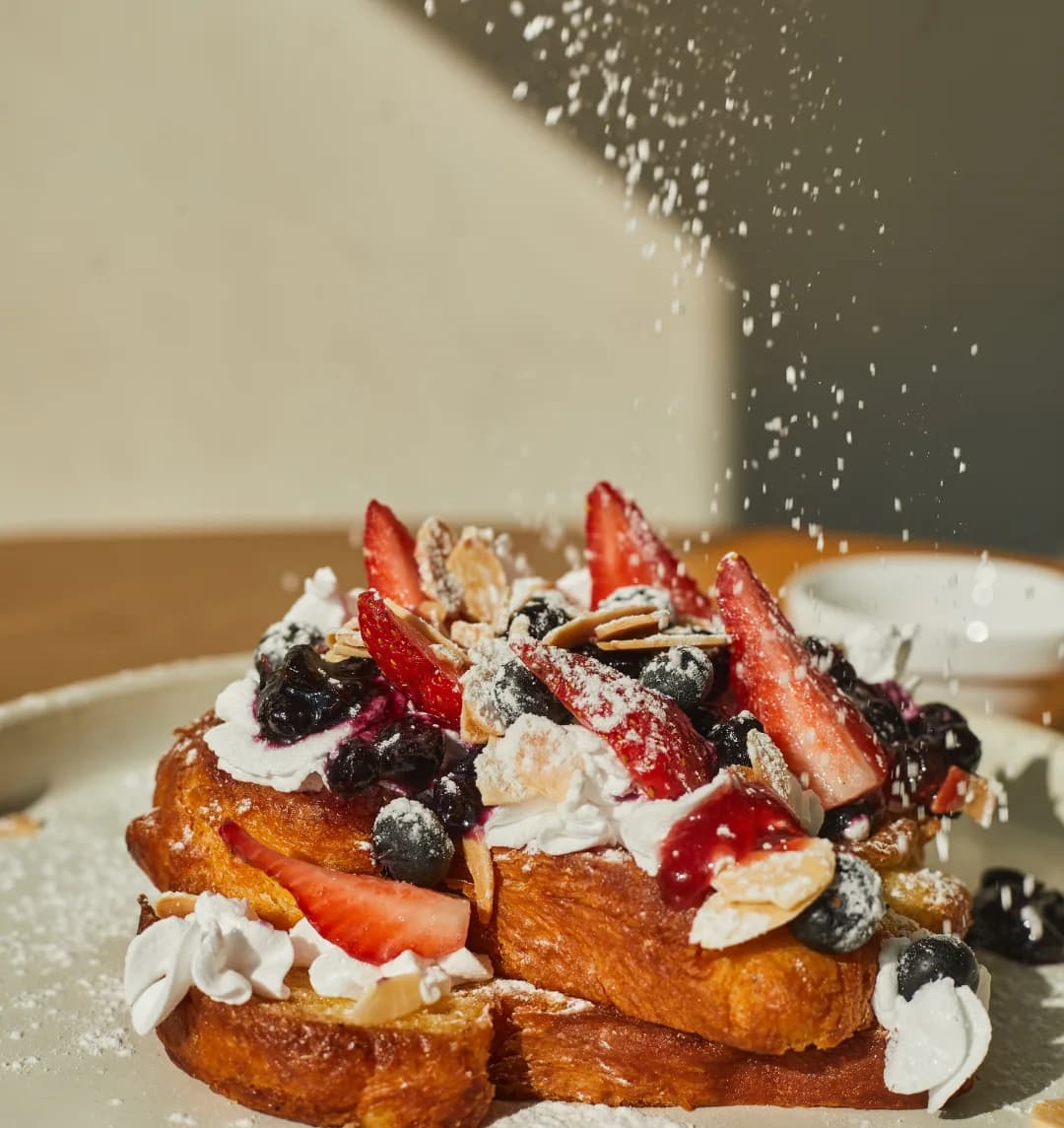 Brioche french toast piled with cream, berries and toasted almonds, dusted with icing sugar