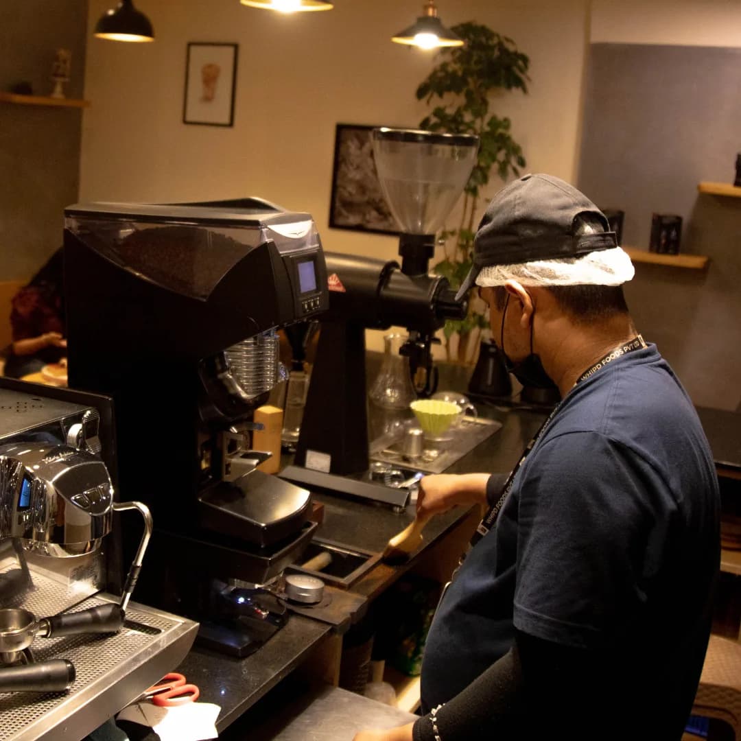 A barista working the grinder station under a warm pendant light