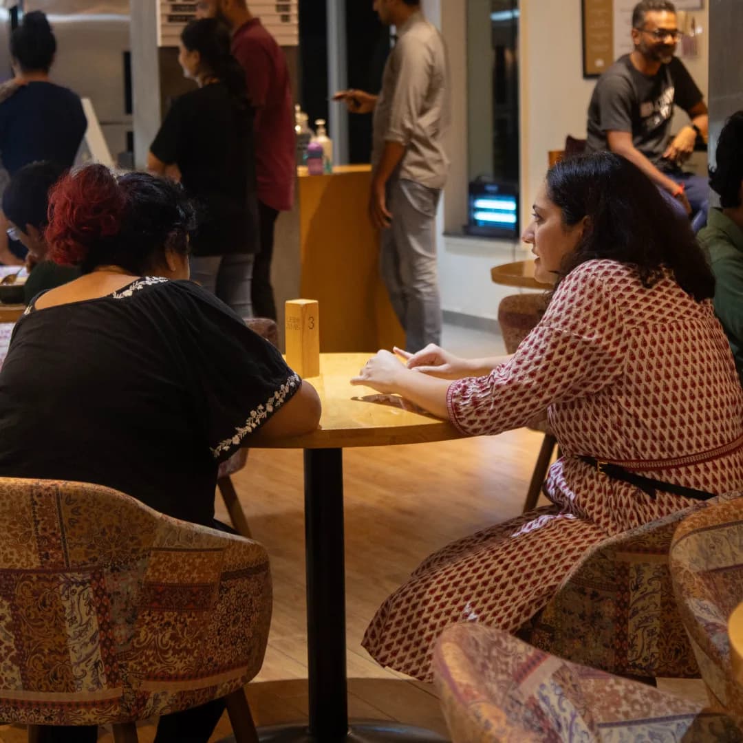 The café floor in the evening, guests at tables under low warm light