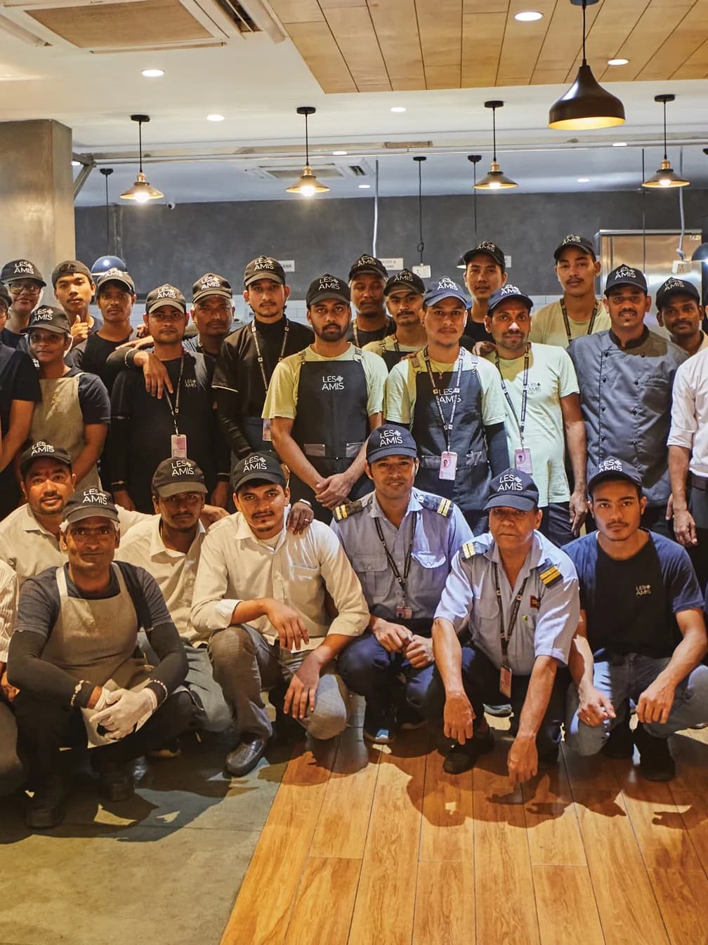 The Les Amis front-of-house team in branded caps and aprons under the pendant lights