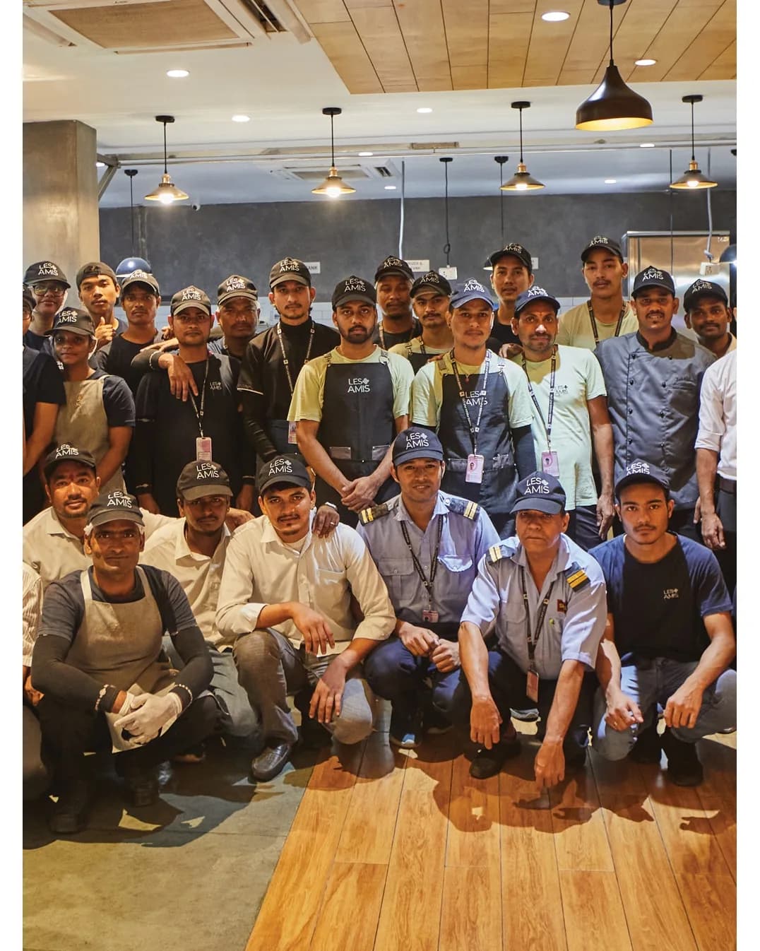 The Les Amis front-of-house team in branded caps and aprons under the pendant lights