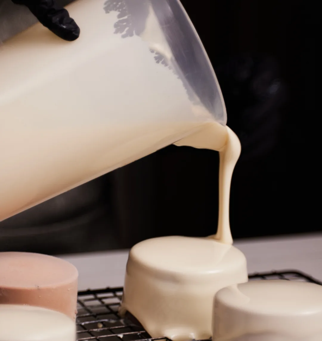 White glaze being poured over a row of petit gâteaux